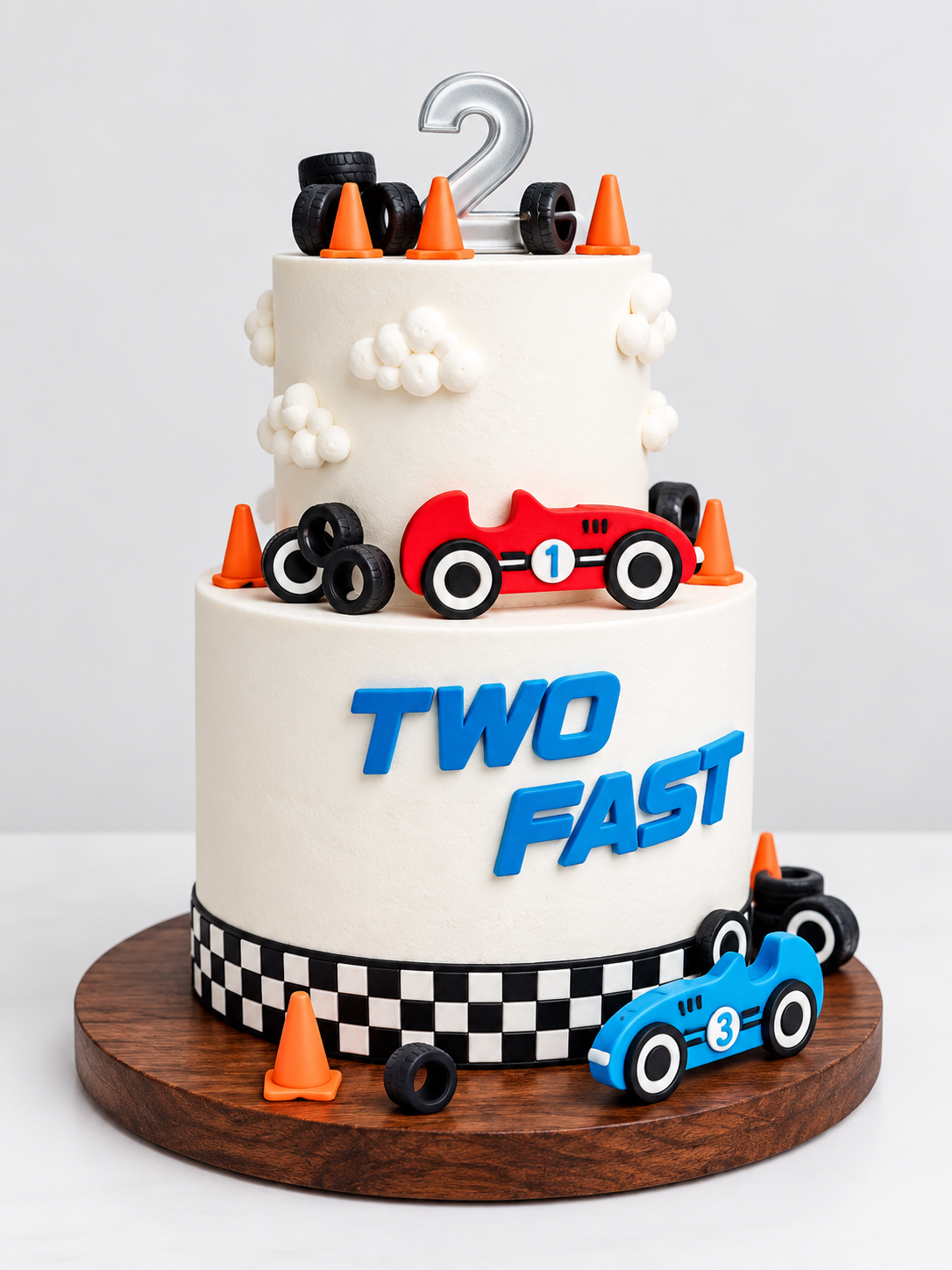 Pastel de dos pisos con temática de carreras, coches rojo y azul, bandera de meta y topper del número 2