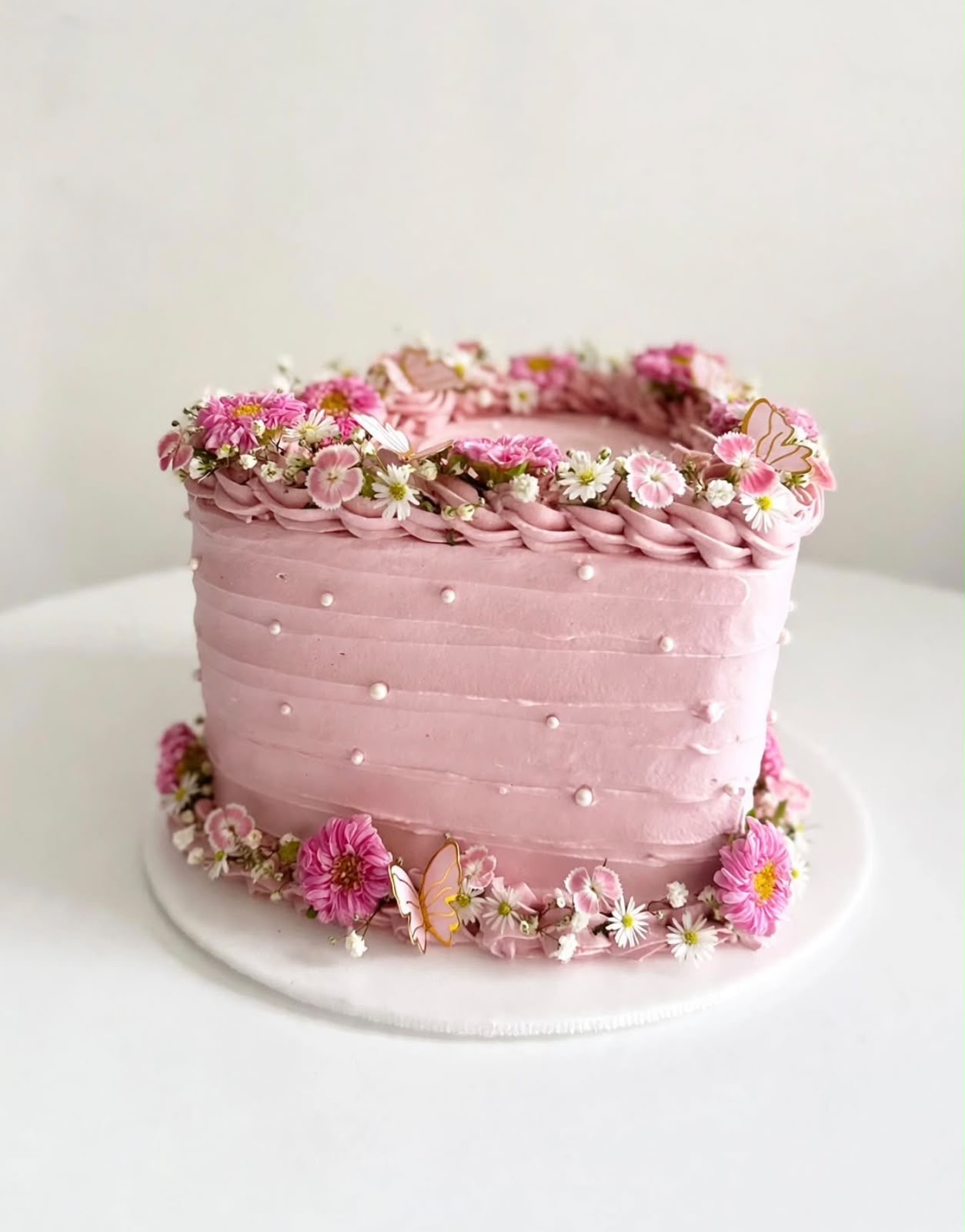 Pastel rosado con crema texturizada, perlas y flores naturales alrededor