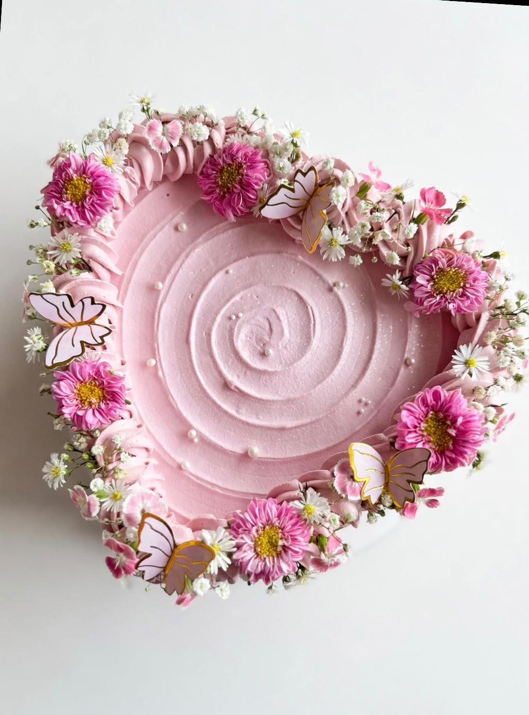 Pastel en forma de corazón con crema rosada, flores naturales y mariposas de azúcar